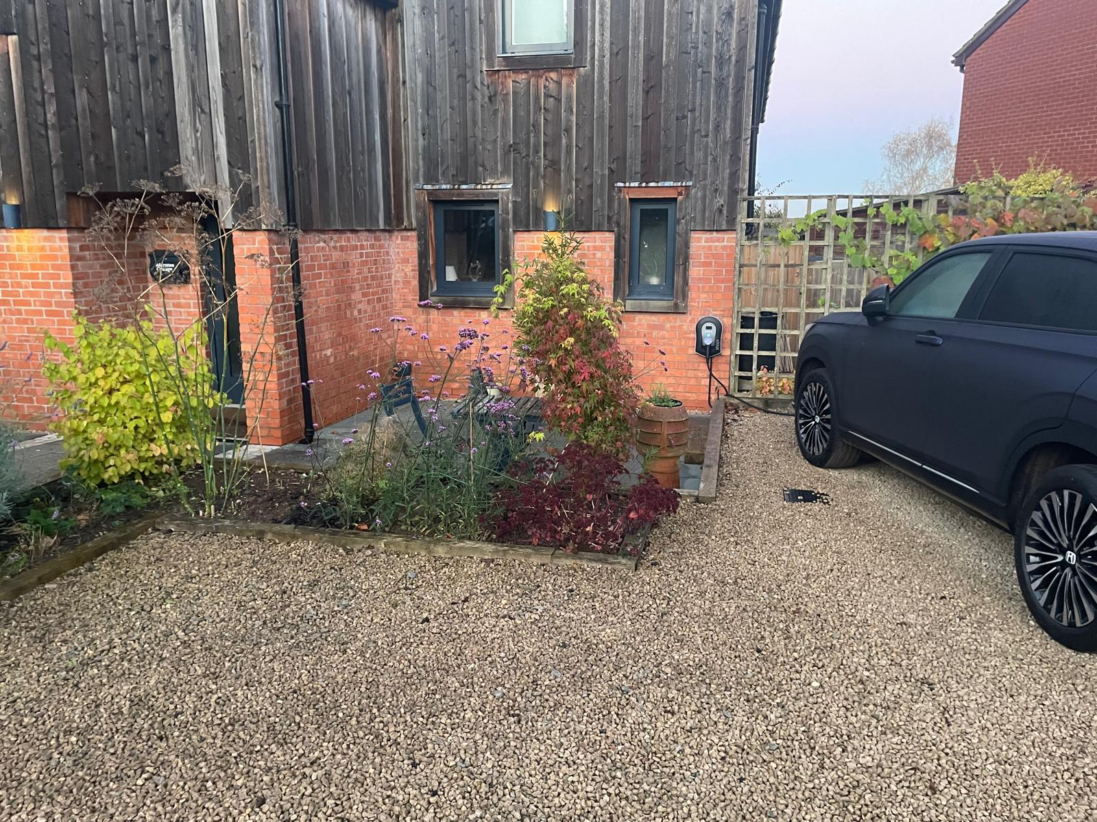 EV charger in a driveway with an electric vehicle plugged in and charging
